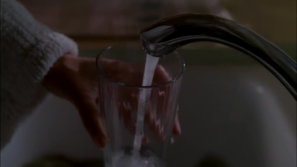 SUSAN stands at the kitchen counter, filling a glass filled with water.jpg